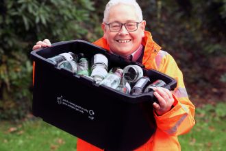 Councillor Edward Thomas in a hi-vis jacket holding a black recycling box filled with glass bottles and jars