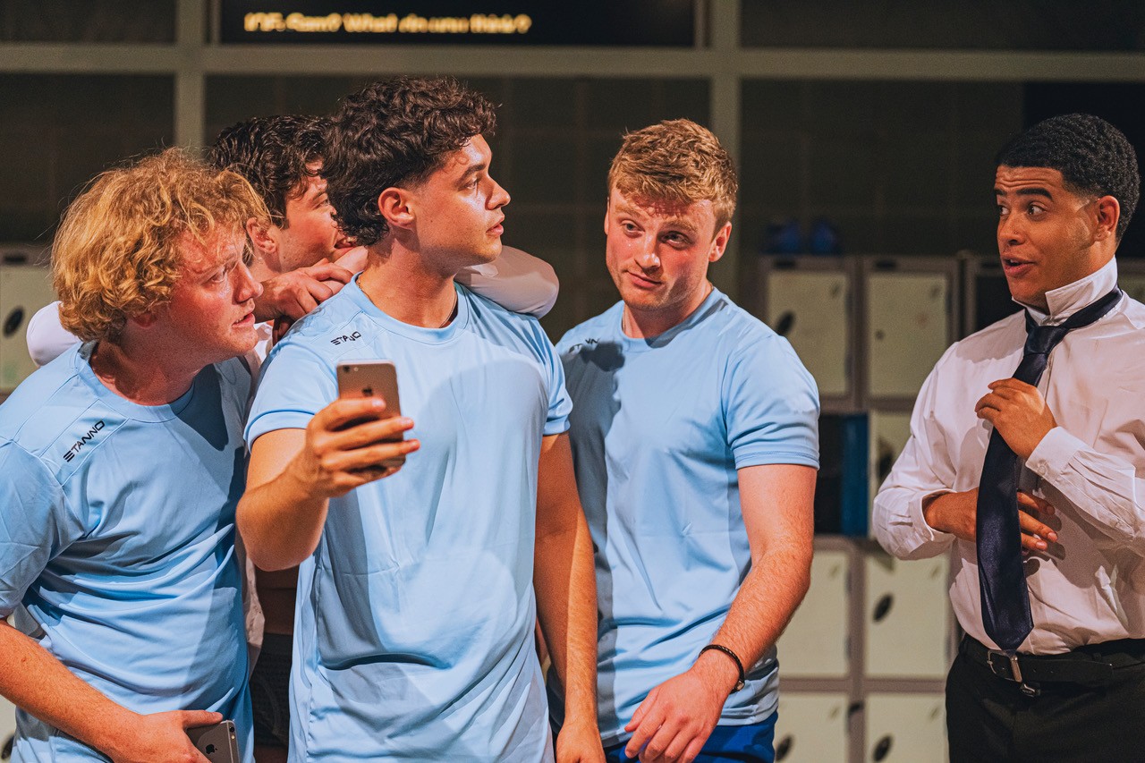 Two performers face each other in a locker room in a tense scene from Physical Education