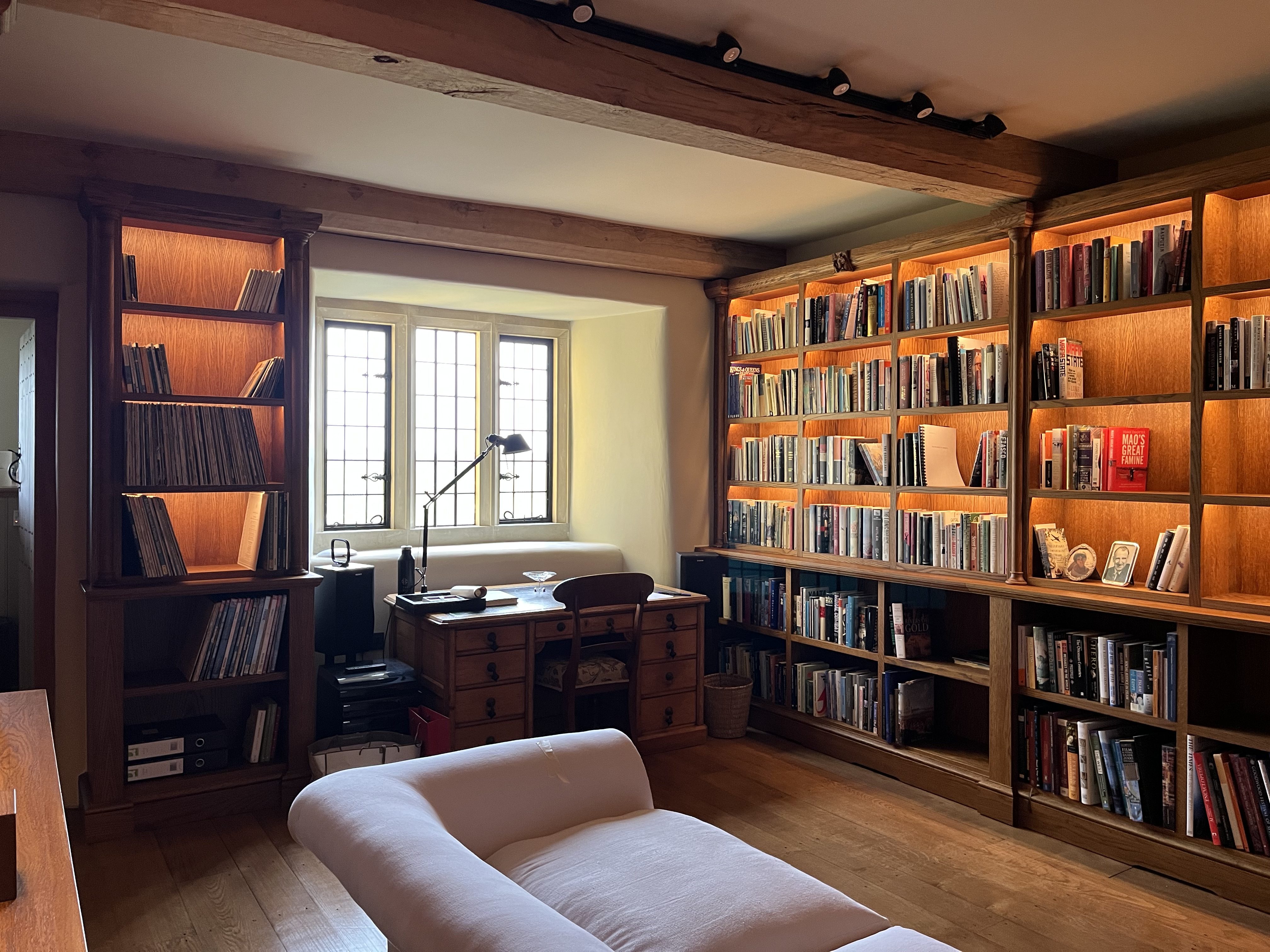 A book-lined study at Sker House with backlit oak shelving, a leaded window and a writing desk