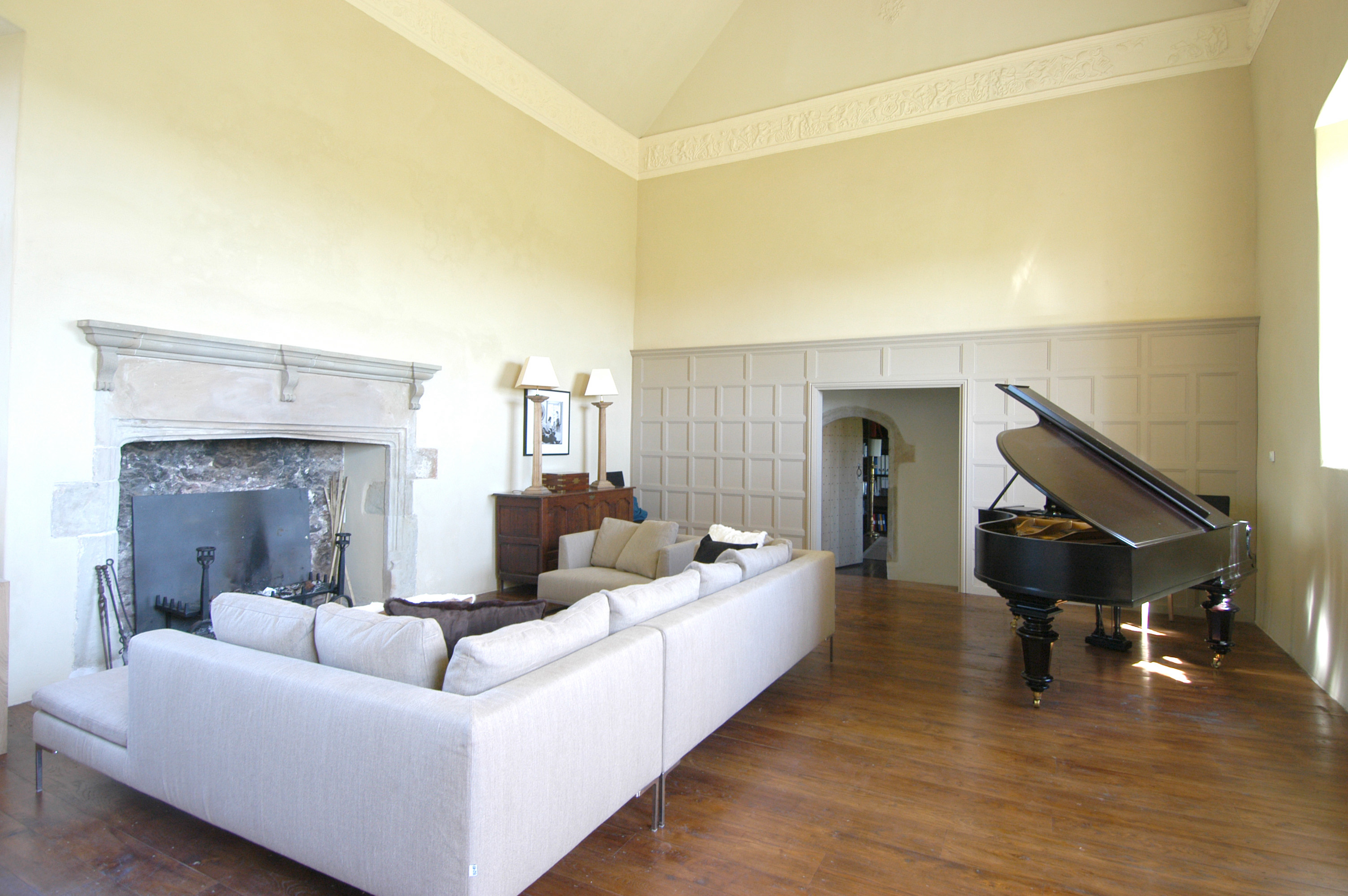 The great hall at Sker House with a vast stone fireplace, decorative plaster frieze, panelled walls and a grand piano