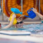 Three children playing with watering cans in a swimming pool