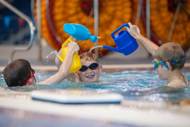 Three children playing with watering cans in a swimming pool