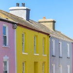 A row of pink, yellow, grey and blue painted terraced houses under a blue sky in Aberaeron