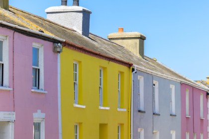A row of pink, yellow, grey and blue painted terraced houses under a blue sky in Aberaeron