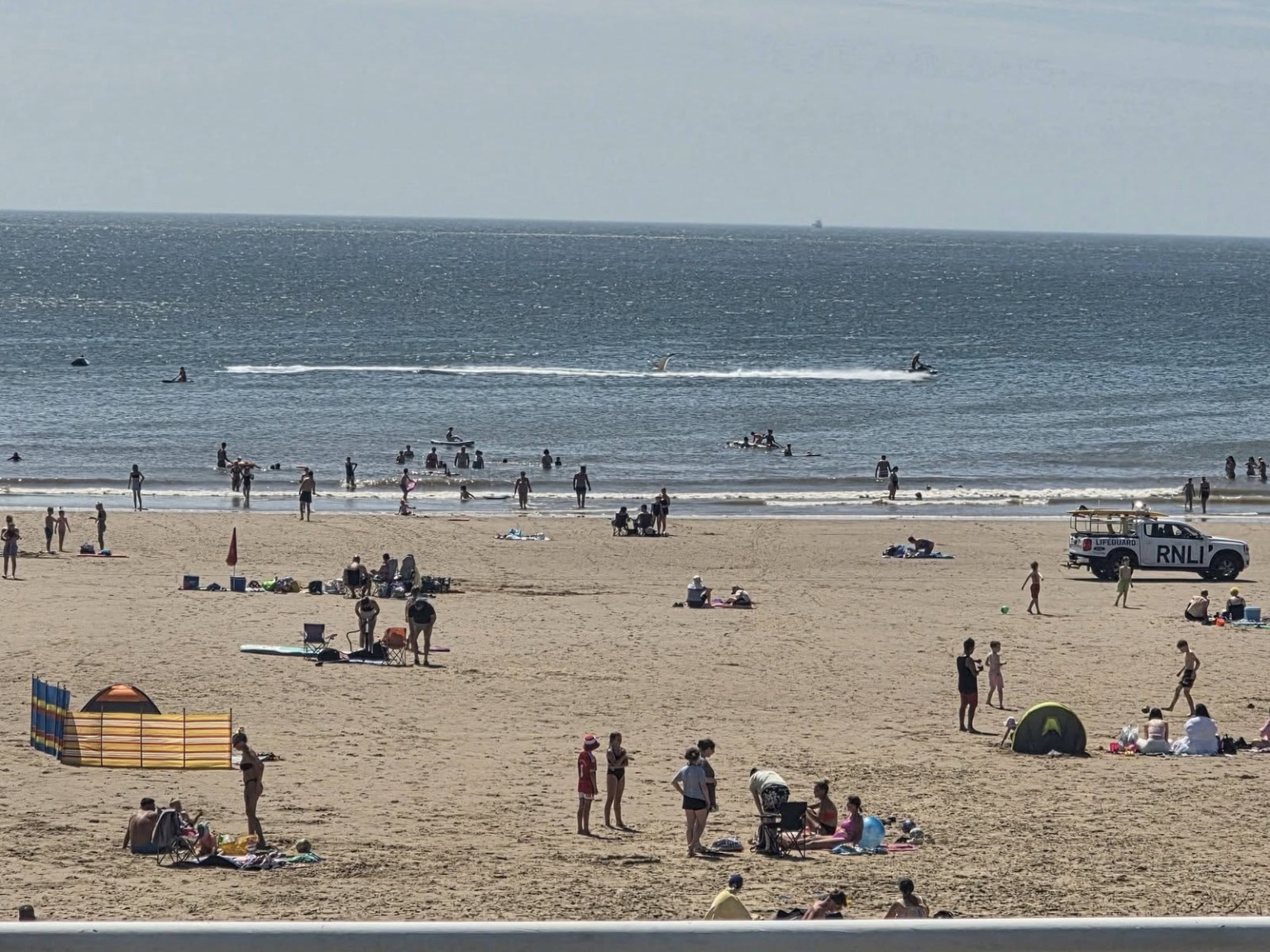 Crowds on the sand and in the sea at Aberavon Beach on a hot summer day, with an RNLI lifeguard truck parked near the shoreline