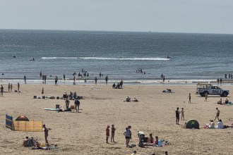 Crowds on the sand and in the sea at Aberavon Beach on a hot summer day, with an RNLI lifeguard truck parked near the shoreline