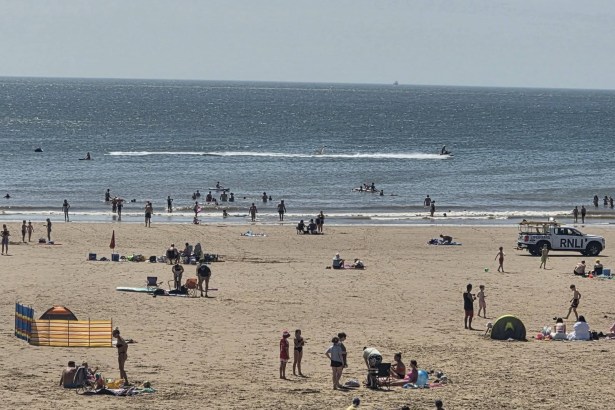 Crowds on the sand and in the sea at Aberavon Beach on a hot summer day, with an RNLI lifeguard truck parked near the shoreline