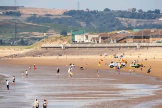 Crowds on the sand at Aberavon Beach on a sunny day, with an RNLI lifeguard vehicle and flags on the beach and the promenade behind