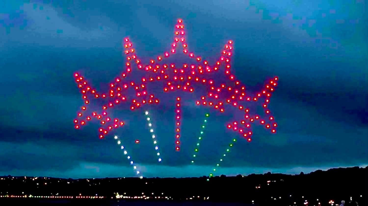 A drone formation forming the Wales Airshow logo in red, with light trails beneath it
