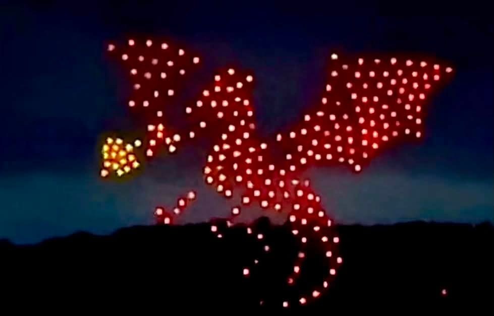 A drone formation in the shape of a red Welsh dragon breathing fire against a dark sky