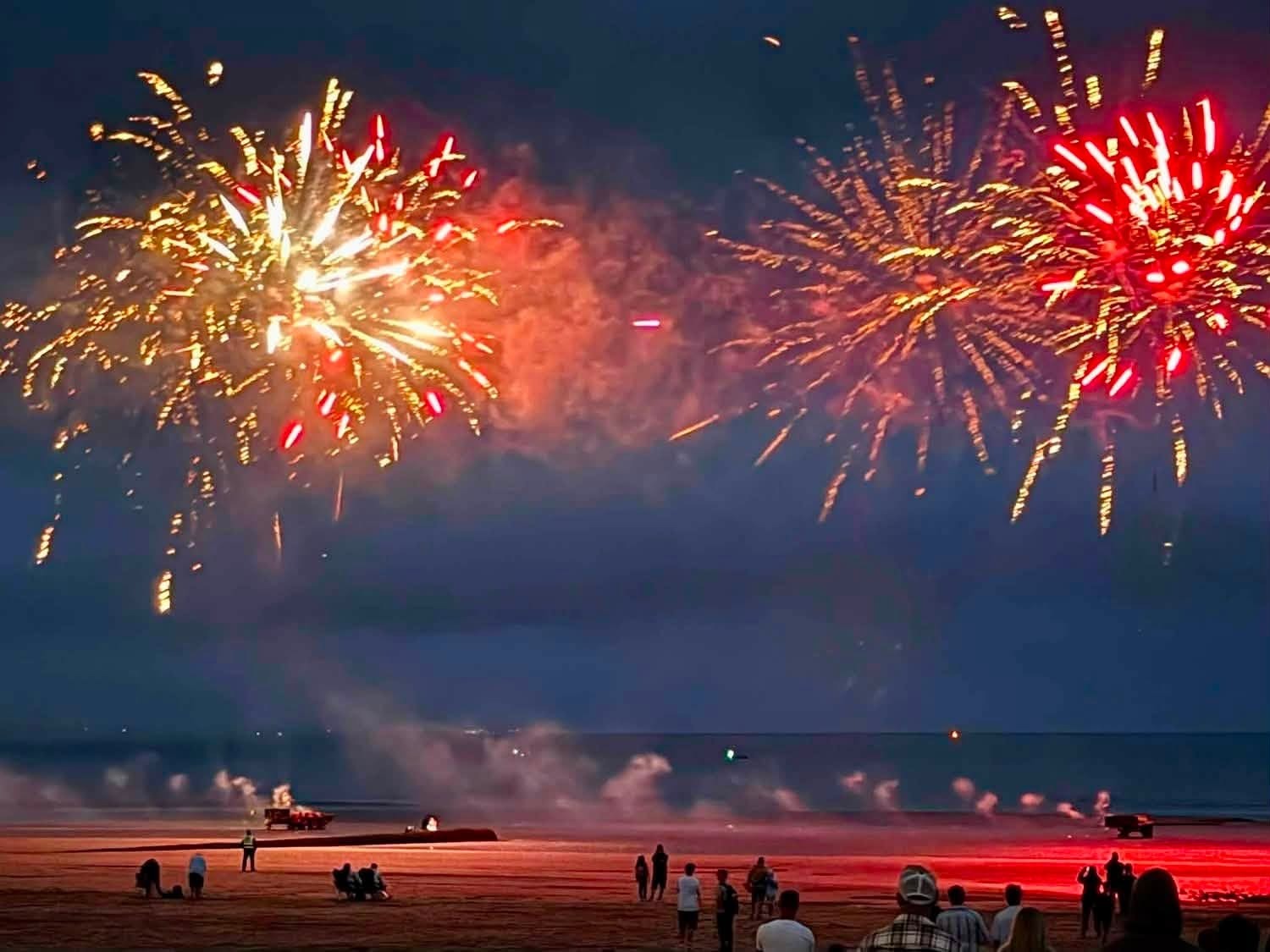 Fireworks bursting over Swansea beach with crowds silhouetted on the sand below