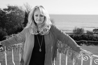 Bonnie Tyler standing on a balcony overlooking the sea, in a black and white photograph