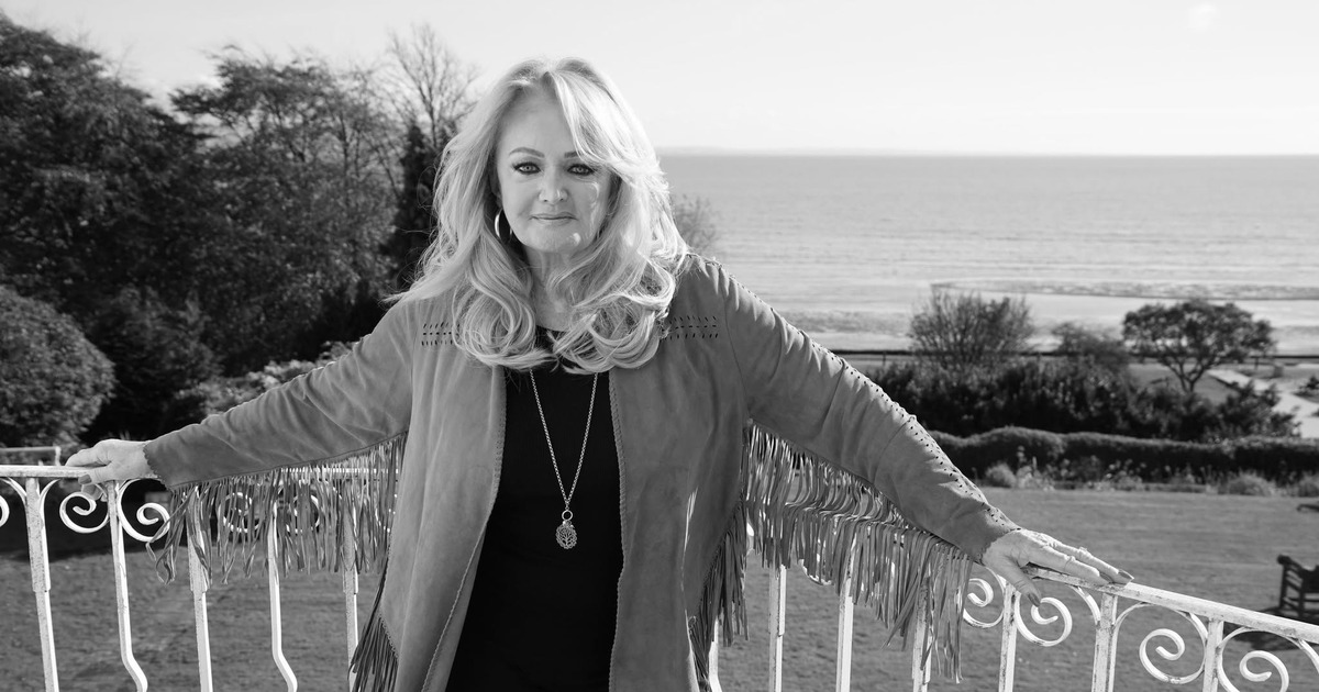 Bonnie Tyler standing on a balcony overlooking the sea, in a black and white photograph