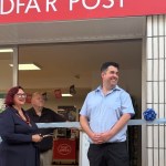 The deputy mayor holding scissors to a light blue ribbon outside the new Bridgend Post Office, with the postmaster and council leader either side under the red bilingual Post Office sign