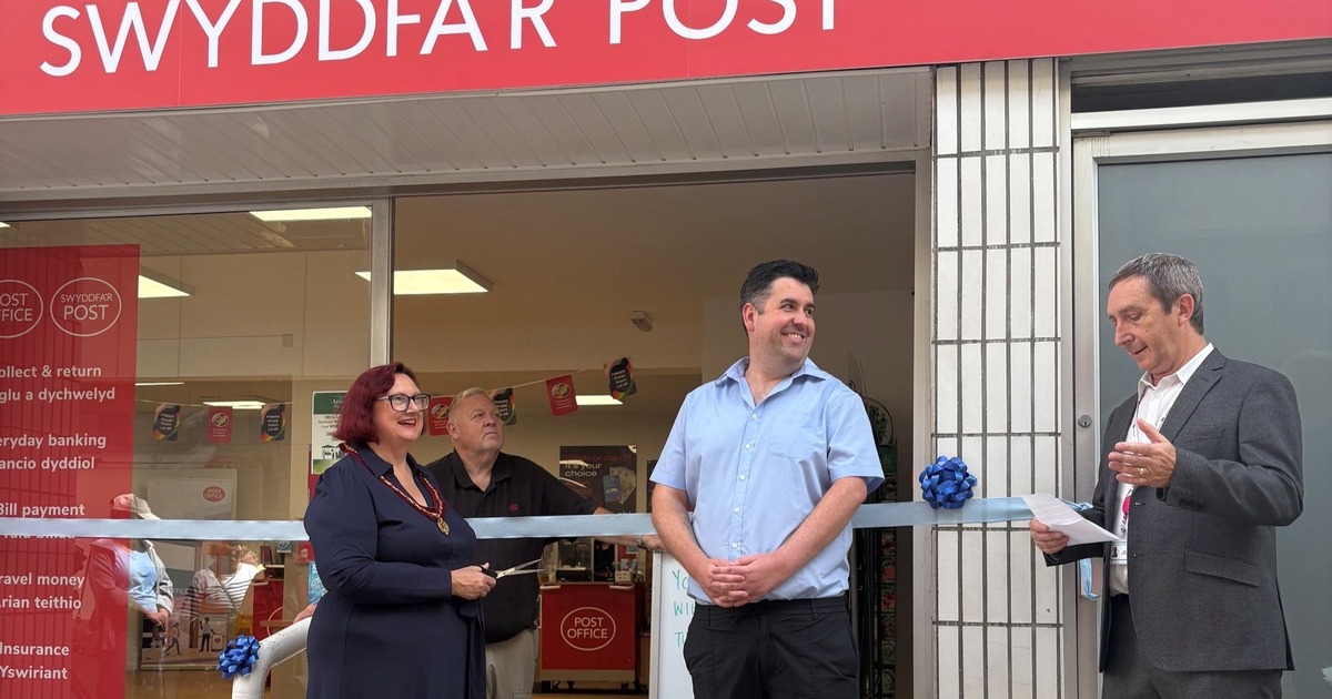 The deputy mayor holding scissors to a light blue ribbon outside the new Bridgend Post Office, with the postmaster and council leader either side under the red bilingual Post Office sign