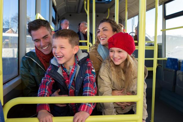 A family of four smiling on board a bus, with the two children looking out of the window