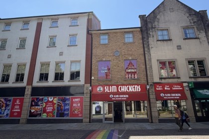The former Carl's Jr unit on Wind Street, Swansea, with Slim Chickens window vinyls covering the frontage and a rainbow crossing in the foreground, next to the trading Slim Chickens restaurant