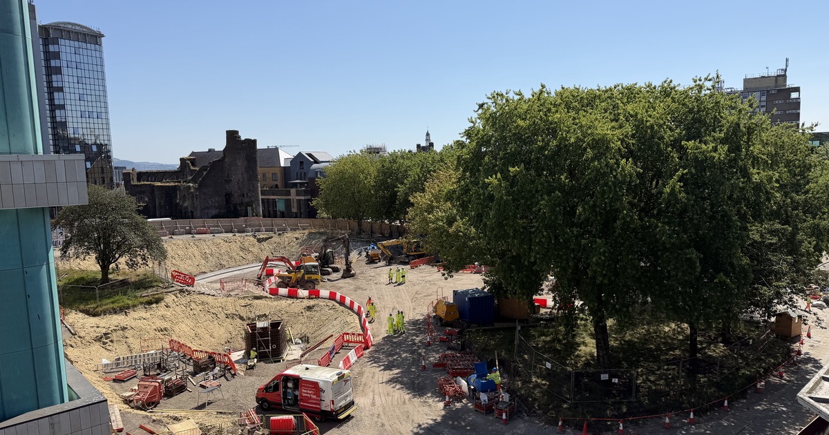 Aerial view of the excavated Castle Square construction site in Swansea, with diggers at work and Swansea Castle in the background