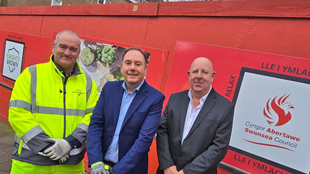 Rob Stewart, David Hopkins and Tim Waller standing in front of the red bilingual site hoardings at Castle Square