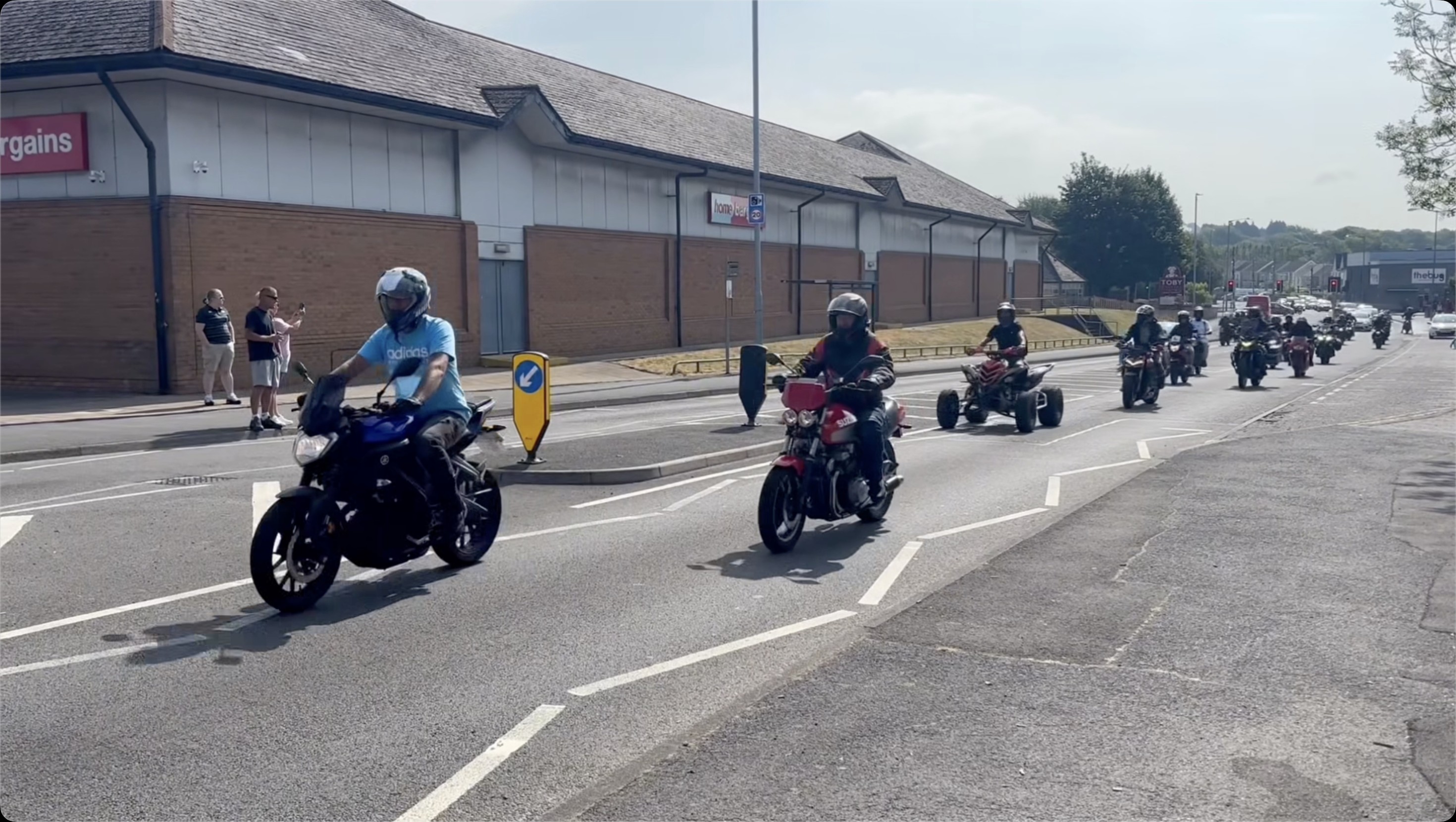Motorbikes and a quad bike riding along the road past a retail park during the memorial ride-out