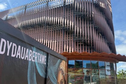 The Copr Bay North multi-storey car park with its rippled copper-coloured louvre facade, seen past a mural hoarding reading Dyddiau Da Abertawe