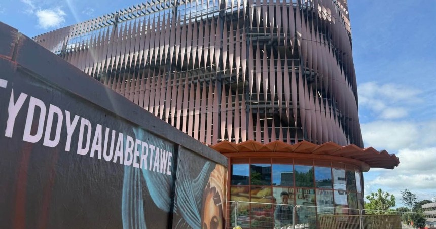 The Copr Bay North multi-storey car park with its rippled copper-coloured louvre facade, seen past a mural hoarding reading Dyddiau Da Abertawe