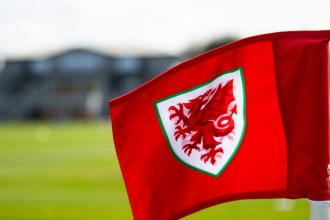 A red corner flag carrying the Cymru dragon crest at the FAW's training ground.