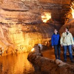 A woman and two children walking beside an underground river inside the floodlit Dan-yr-Ogof showcaves