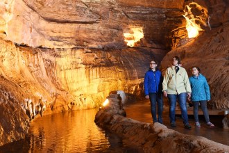 A woman and two children walking beside an underground river inside the floodlit Dan-yr-Ogof showcaves