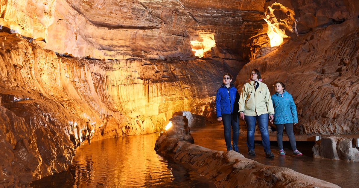 A woman and two children walking beside an underground river inside the floodlit Dan-yr-Ogof showcaves