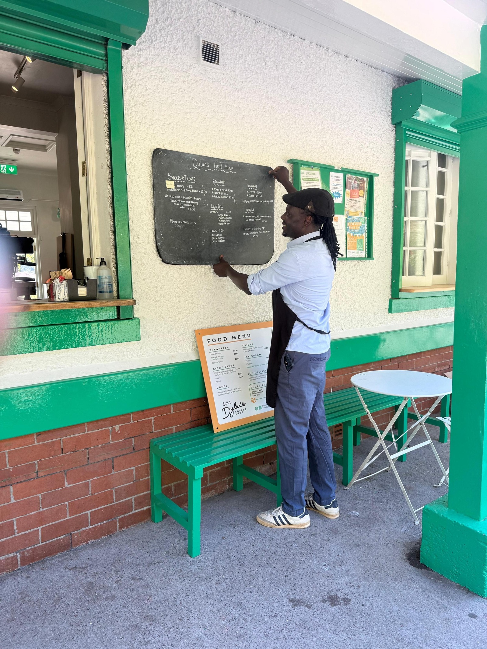 A man in an apron hanging the food menu blackboard on the coffee shop's wall