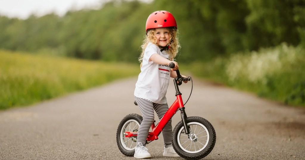 A young girl in a red helmet riding a red Cycle Champs balance bike along a country path