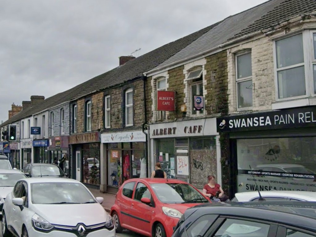 A parade of shops on High Street in Gorseinon including Albert's Cafe, The Shoetree and Swansea Pain Relief with cars parked outside