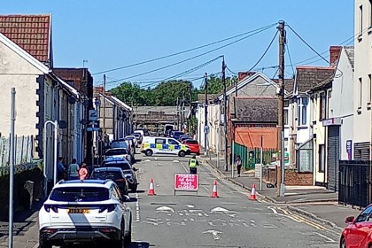 A road closed sign and traffic cones blocking a residential street in Gorseinon, with a police van beyond the cordon