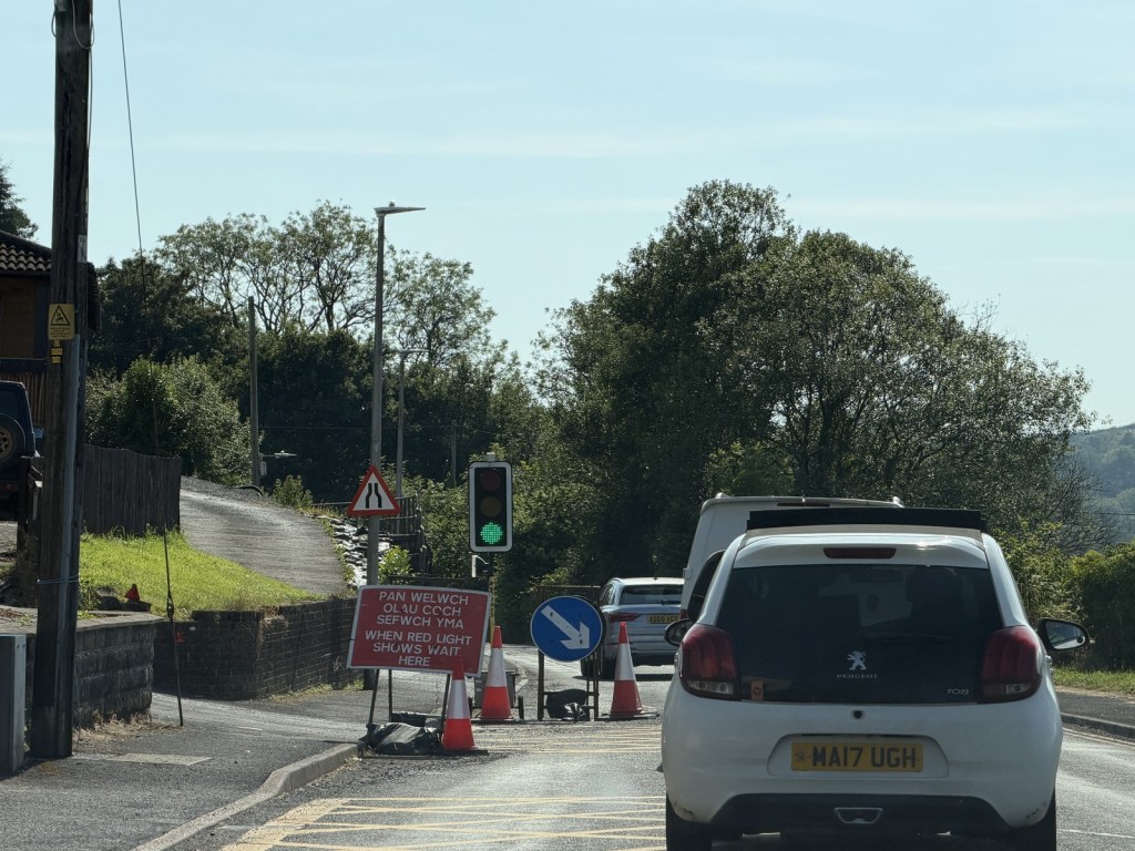 Temporary traffic lights on green on the B4317, with a red bilingual sign instructing drivers to wait at the line.