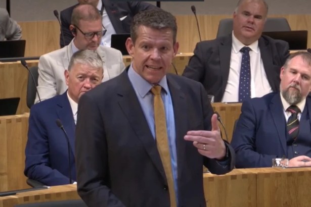 Rhun ap Iorwerth speaking in the Senedd chamber, gesturing, with MSs seated behind him.