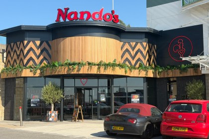 The new Nando's restaurant at Parc Fforestfach in Swansea, with red Nando's lettering above a curved timber frontage, black and tan chevron panelling and a red neon cockerel logo on the wall
