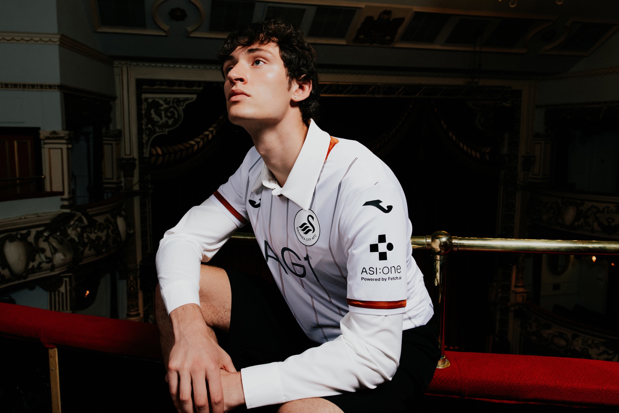 A model in the new Swansea City home shirt with a collared shirt underneath, seated by the Grand Theatre balcony rail
