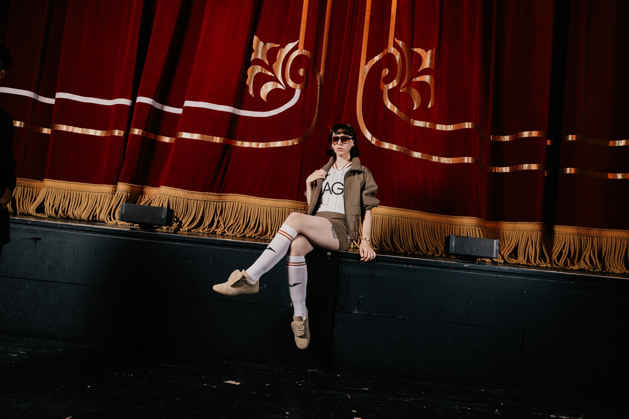 A model in the new Swansea City home shirt sitting at the edge of the Grand Theatre stage in front of the red curtain