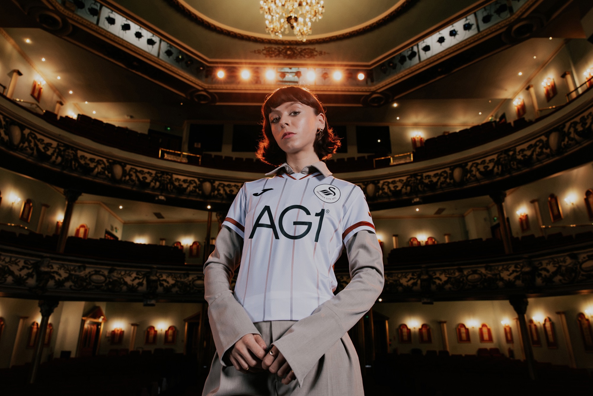 A model wearing the new Swansea City home shirt standing in the Grand Theatre auditorium