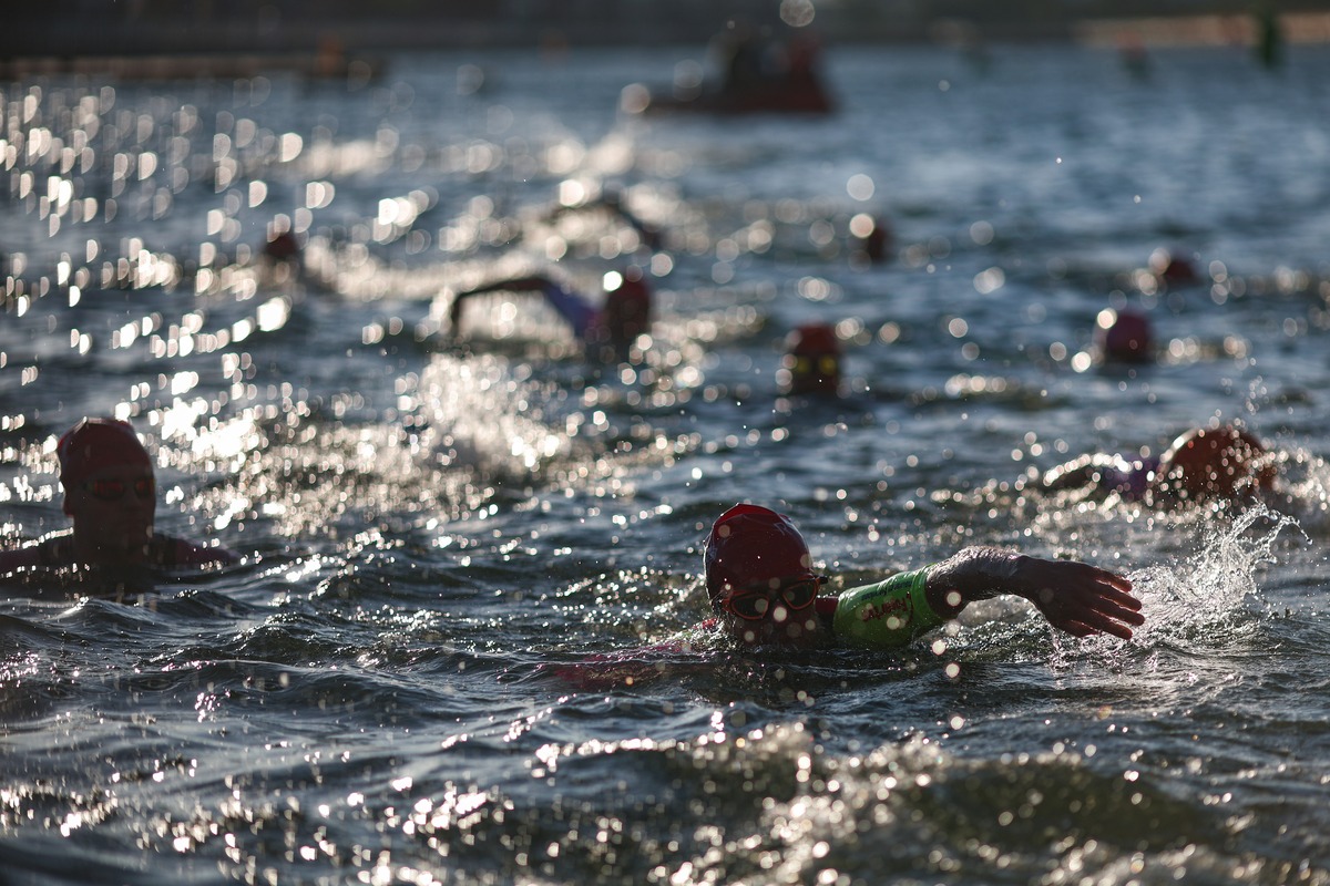 A swimmer in a red cap mid-stroke, backlit by morning sun sparkling on the water