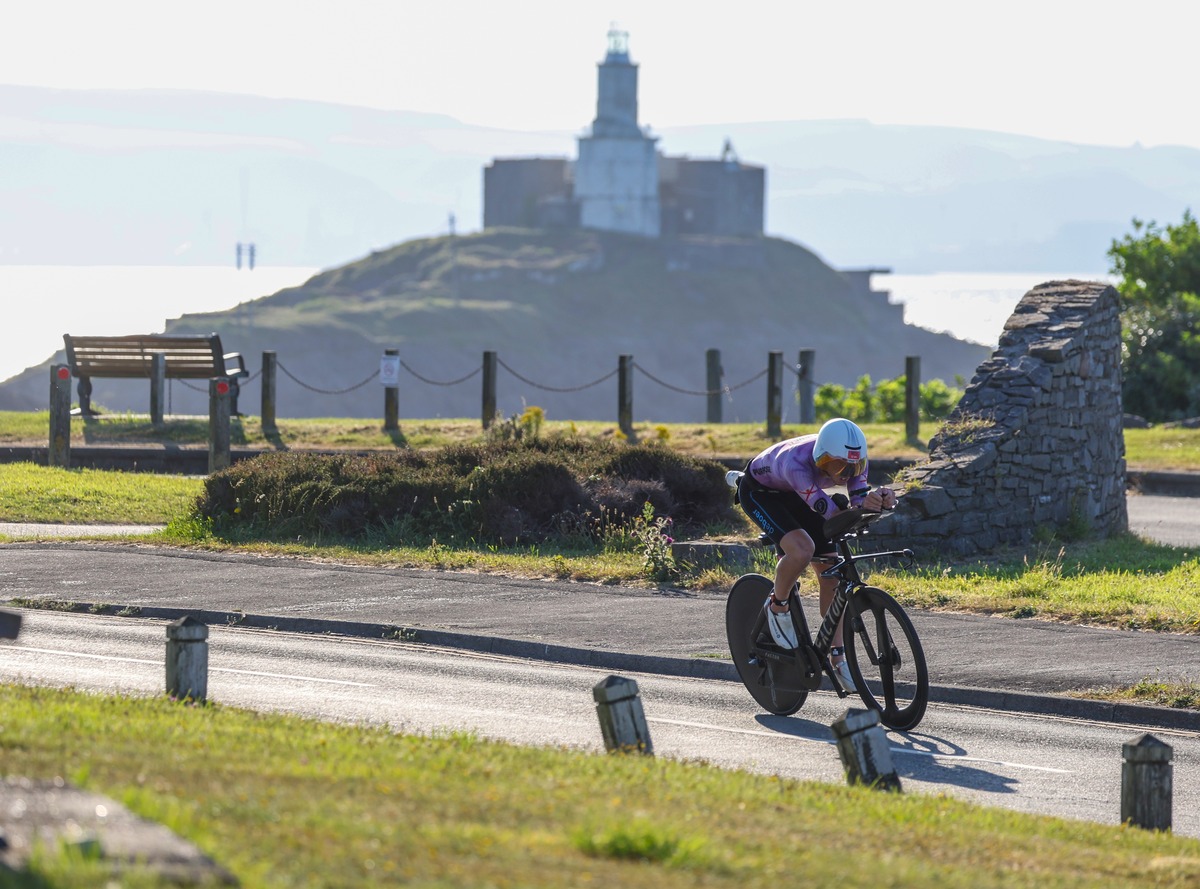 A cyclist in an aero position rides past with Mumbles lighthouse in the background