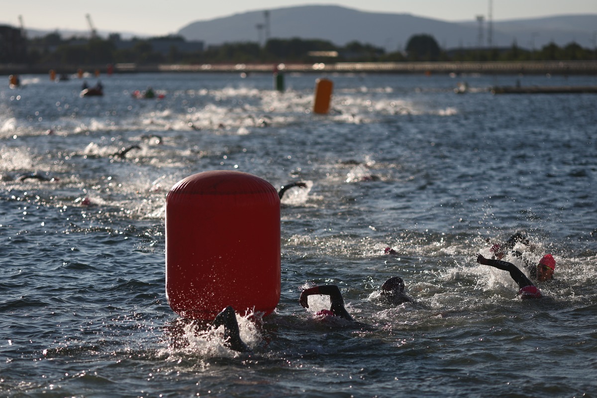 Swimmers in wetsuits and pink caps round a large red buoy in the dock