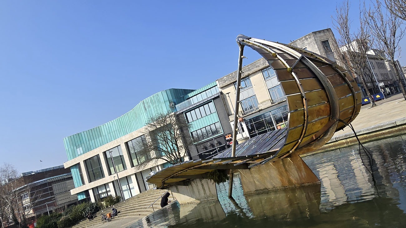The Leaf Boat, a large curved glass and steel sculpture shaped like a leaf, beside the water feature in Swansea's Castle Square
