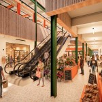 Architect's visualisation of the main entrance atrium inside the proposed Llanelli Market Hall, with orange-framed market stalls, timber-lined balconies and shoppers