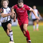 Llanelli Town's Ethan Cann shields the ball from a Haverfordwest County player in a red Reds home shirt at Stebonheath Park