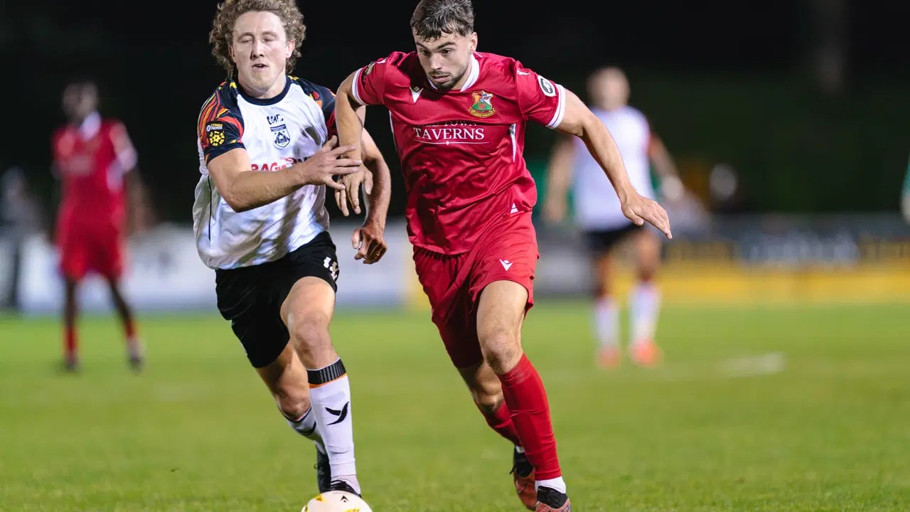 Llanelli Town's Ethan Cann shields the ball from a Haverfordwest County player in a red Reds home shirt at Stebonheath Park
