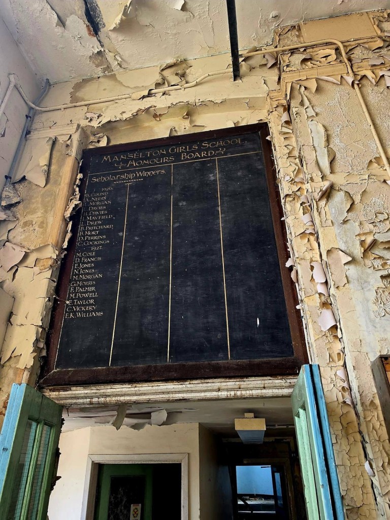Manselton Girls' School honours board with scholarship winners for 1926 and 1927 and empty columns, above a doorway with peeling paint