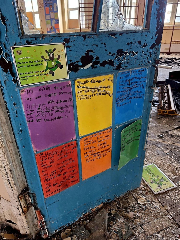 Blue peeling classroom door covered in colourful attendance tally sheets with a school rights poster