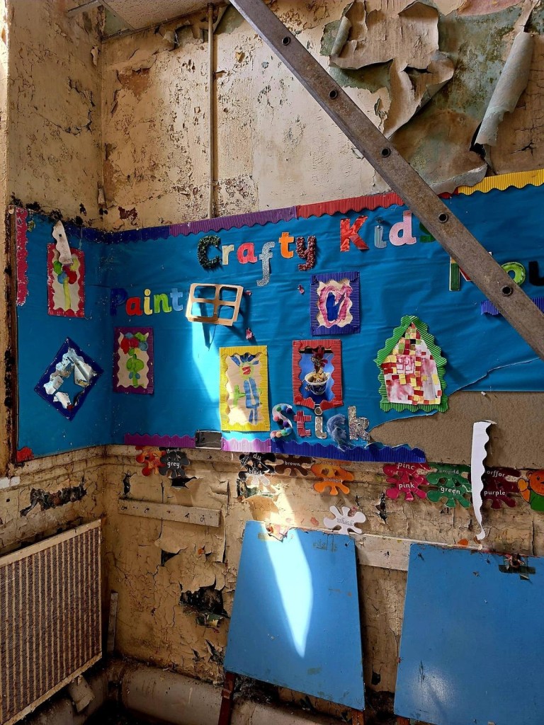 Crafty Kids classroom display with children's paintings on a blue board surrounded by flaking paint
